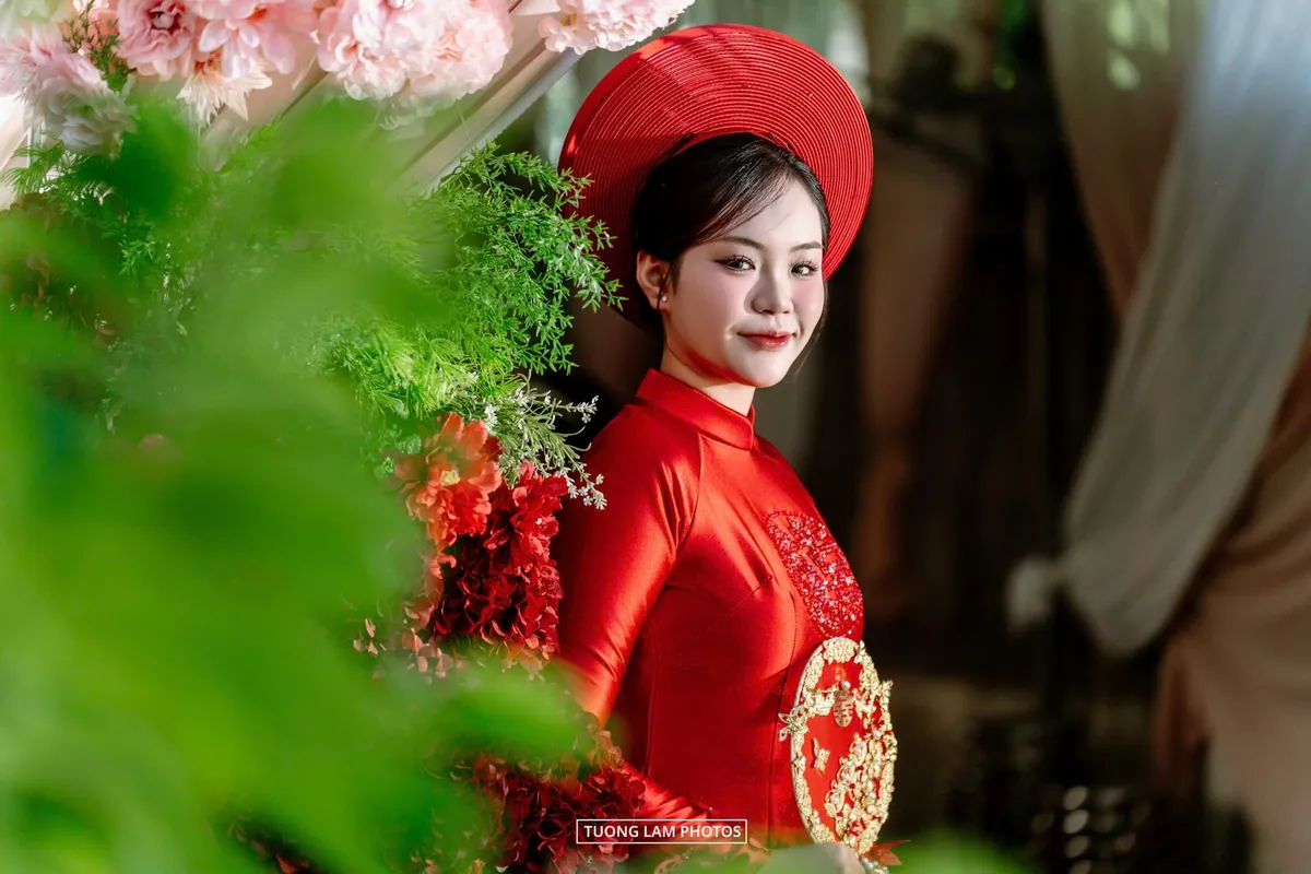 Cô dâu áo dài đỏ đội khăn mấn, góc nghiêng mềm mại giữa hoa lá