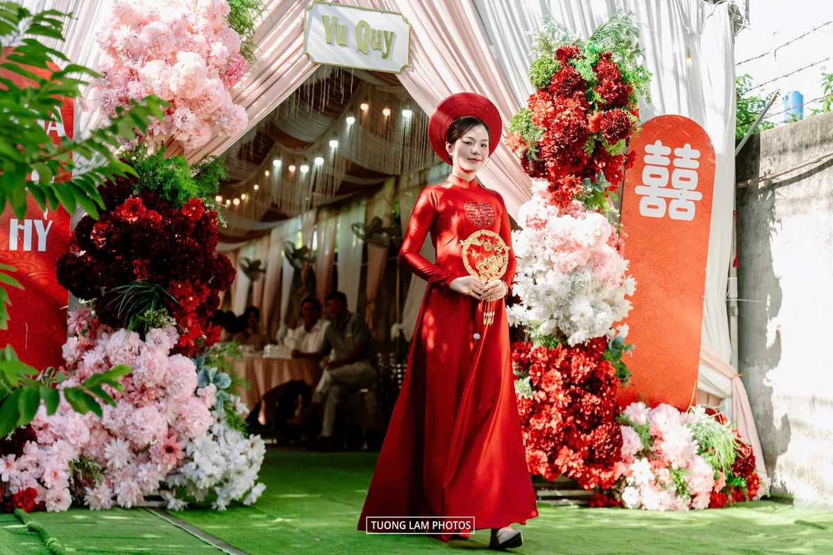Cô dâu áo dài đỏ đứng giữa cổng hoa trong lễ vu quy