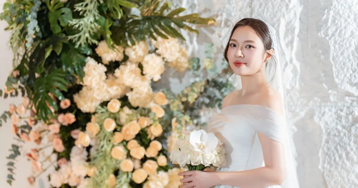 Cô dâu váy cưới trắng cầm hoa đứng giữa vườn hoa trắng